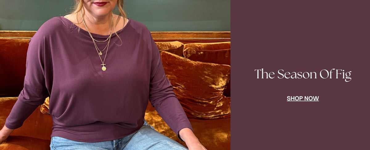 Woman wearing Melyr Aimee batwing top in the colour fig while seated on a velvet couch