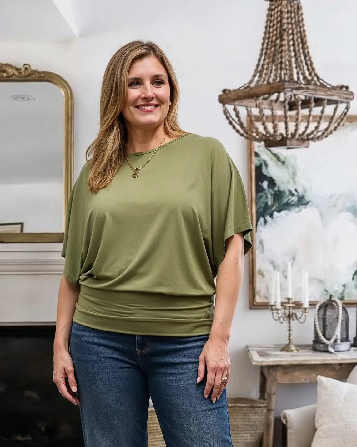 Woman wearing an olive green top and blue jeans standing in a living room.