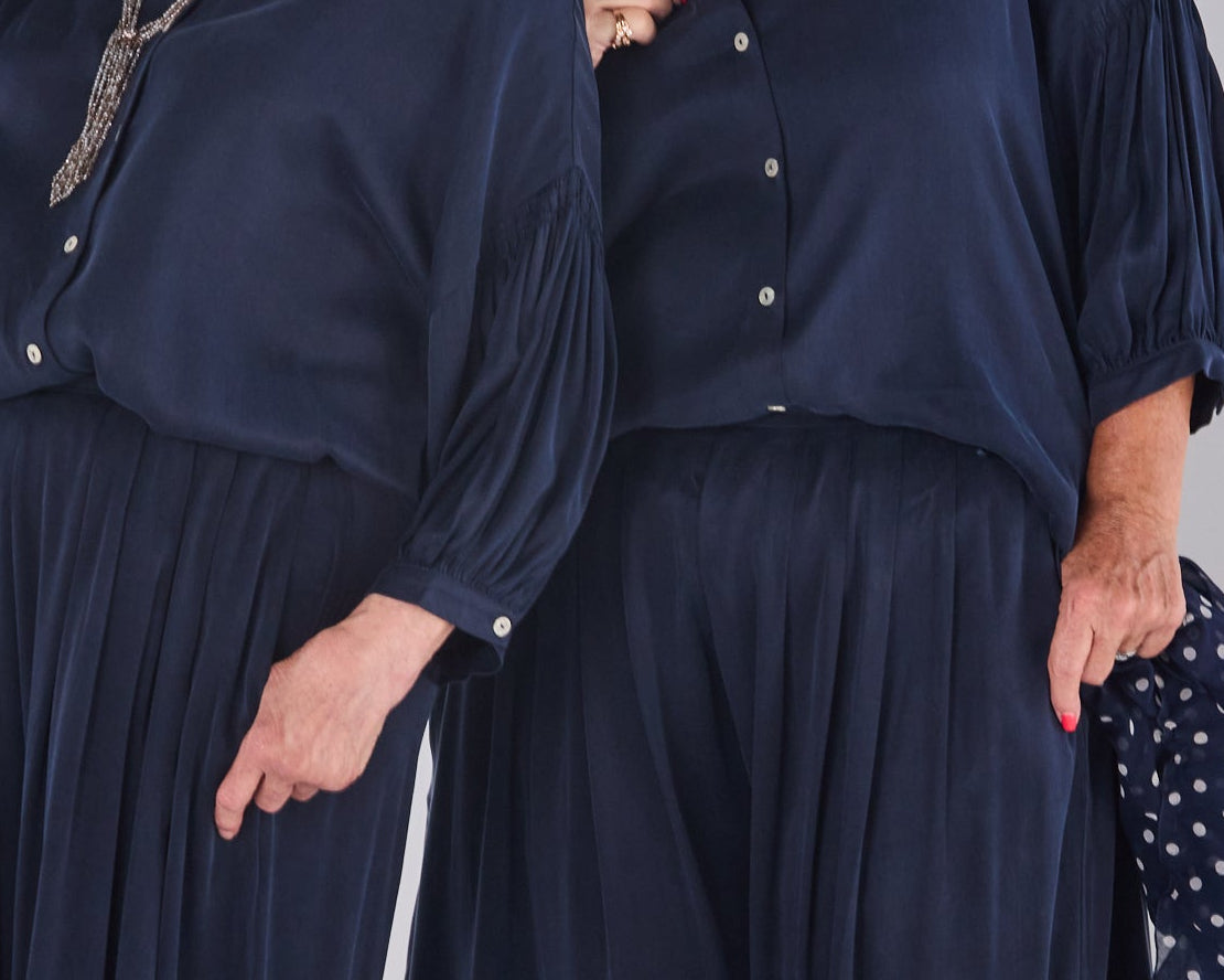 Two women modeling matching Melyr navy blue wide-leg pants and long-sleeve button-front tops against a plain light gray studio background.