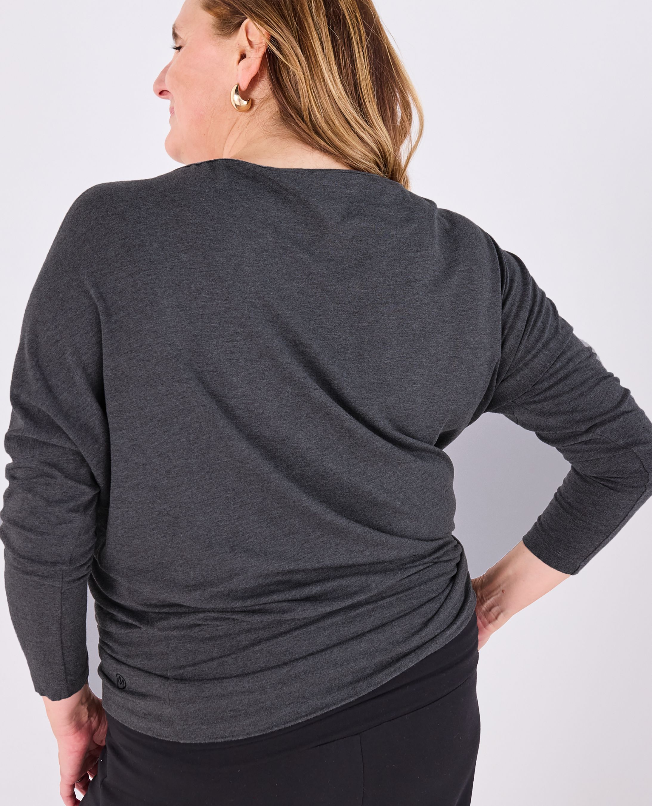 A woman shown from the back wearing a dark gray long-sleeve Melyr Aimee top and black pants against a light gray studio background.