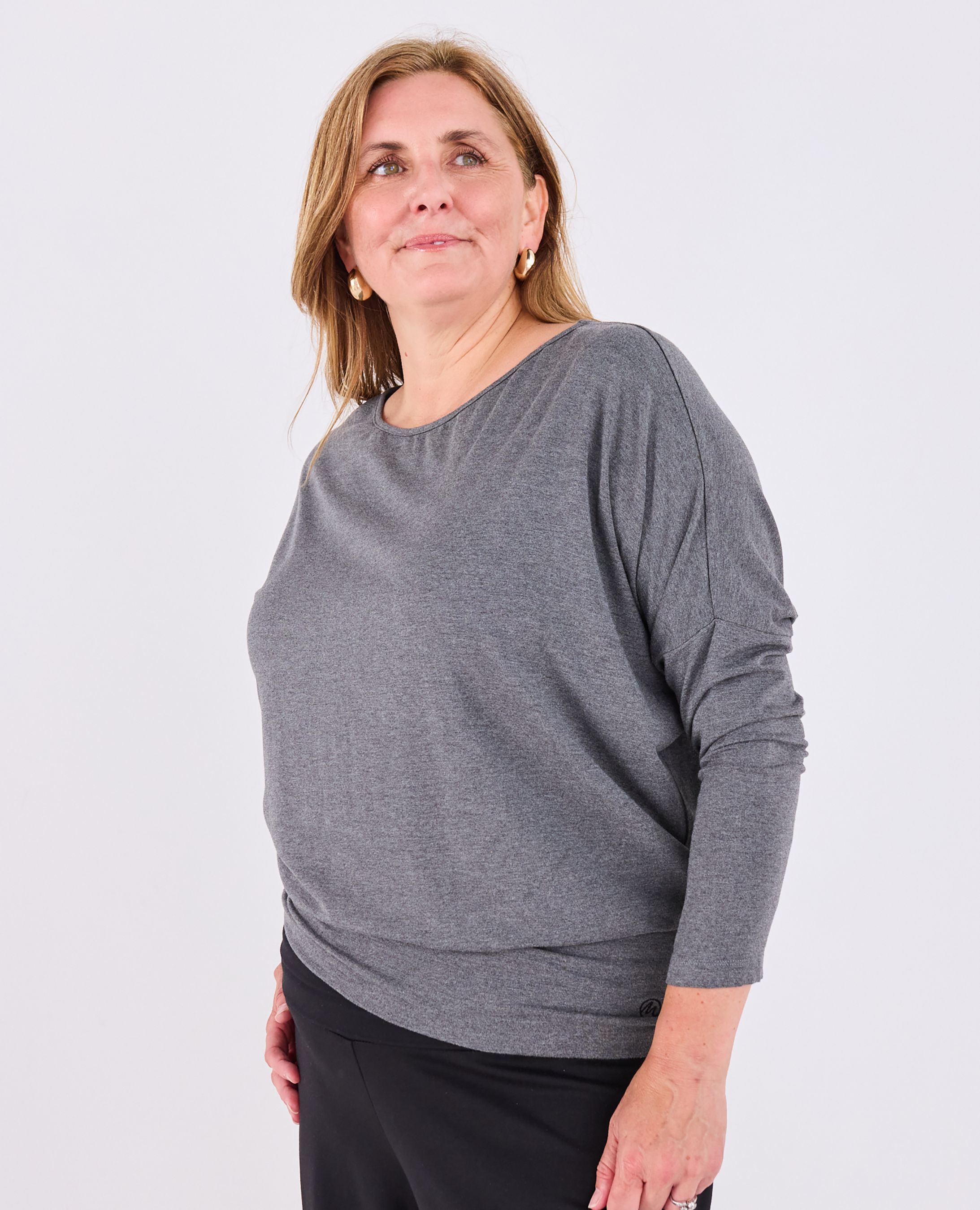 A woman wearing a heather gray long-sleeve Melyr Aimee top with a wide boat neckline, paired with black pants, photographed against a solid light gray background.