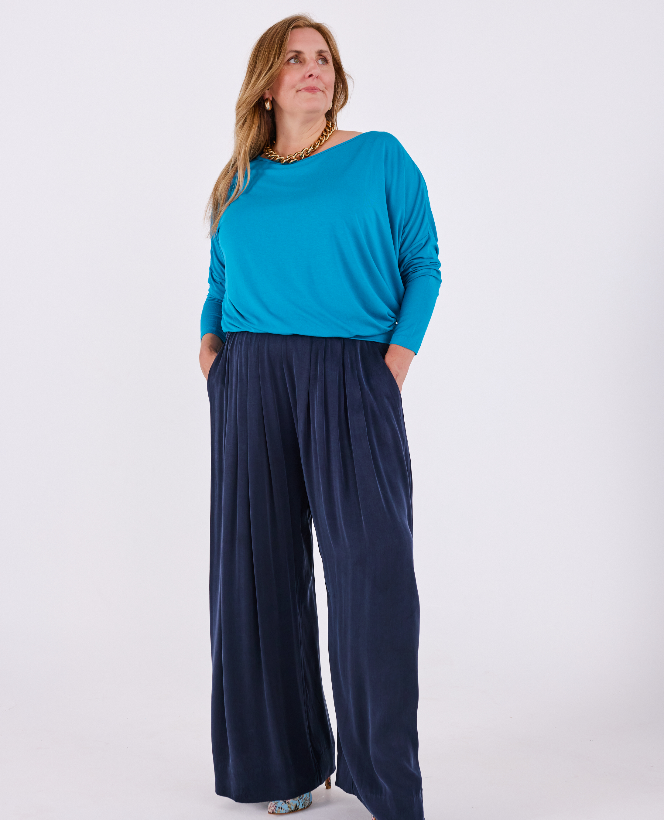 A woman modeling Melyr long-sleeve top and Portofino navy wide-leg pleated pants against a plain white studio background.l