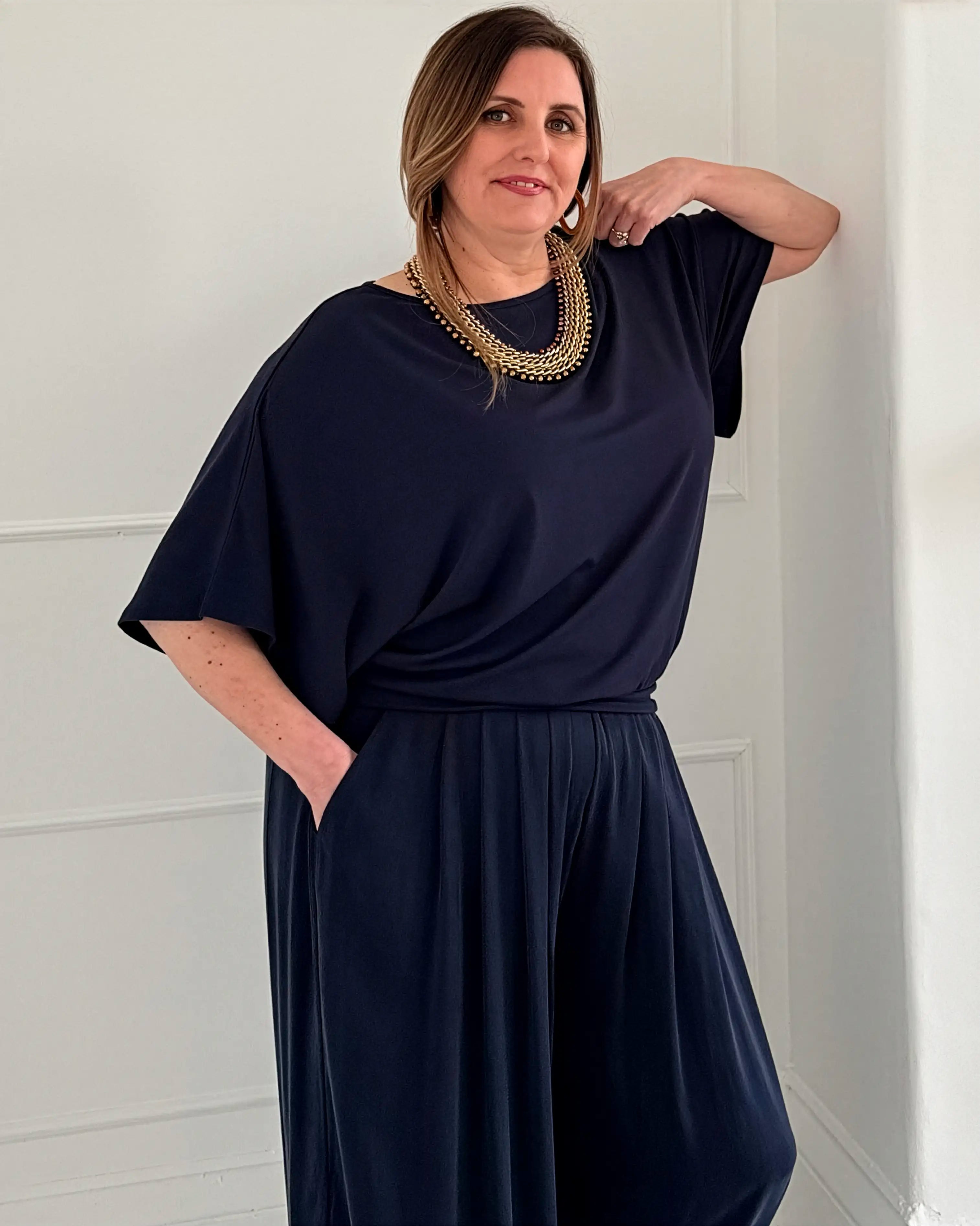 Woman wearing a navy blue Melyr top and trousers with a gold necklace against a white background
