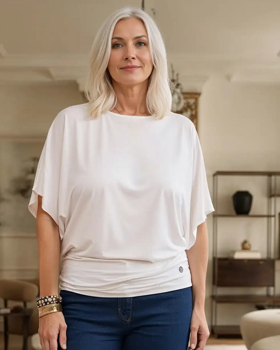 Woman wearing a white Melyr top and blue jeans in an indoor setting