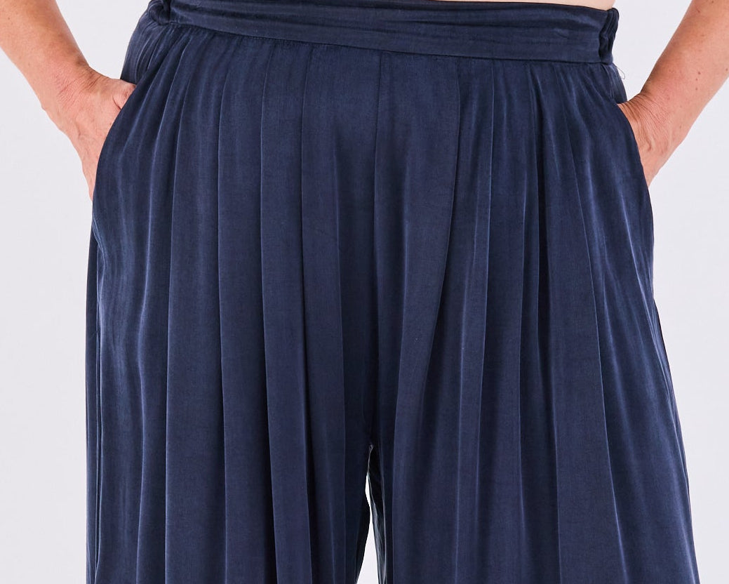 A person wearing Melyr wide-leg pleated pants in dark navy blue, shown from the waist down against a plain light gray studio background.