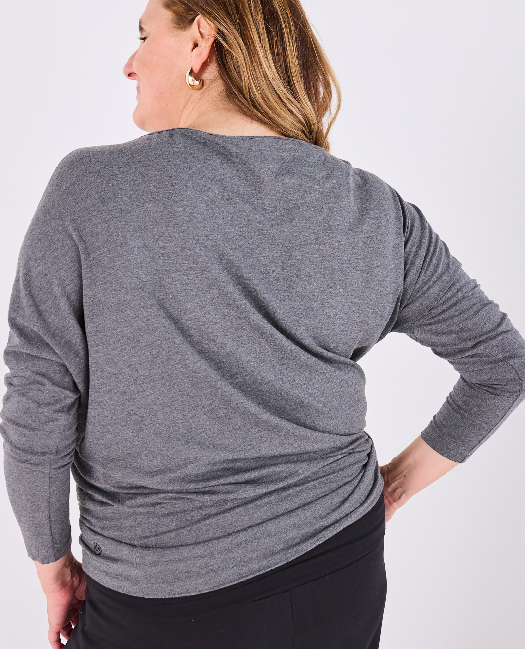 A woman wearing a heather gray long-sleeve top, shown from the back against a light gray studio background.