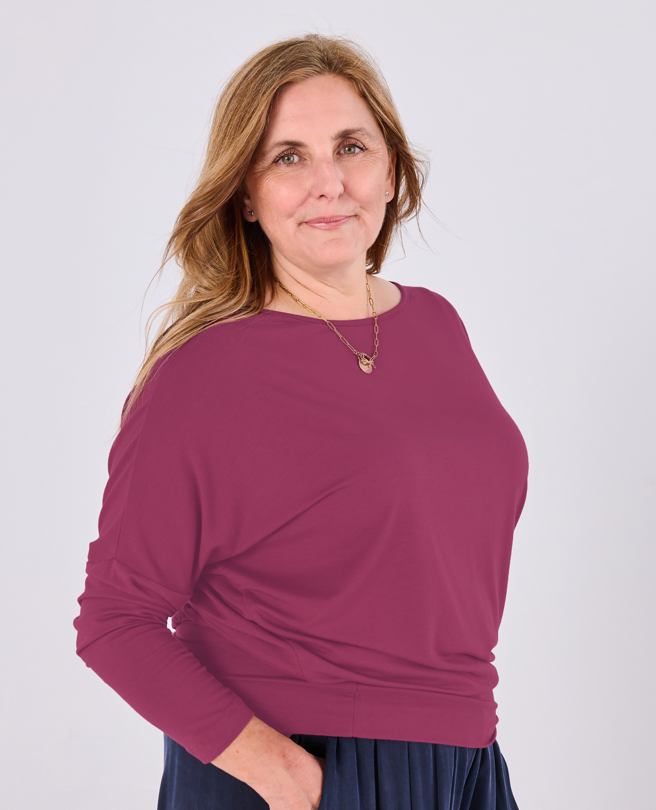 A woman modeling a Melyr Aimee long-sleeve boat-neck knit top in a dusty magenta color, paired with a dark navy skirt, against a light gray studio background.