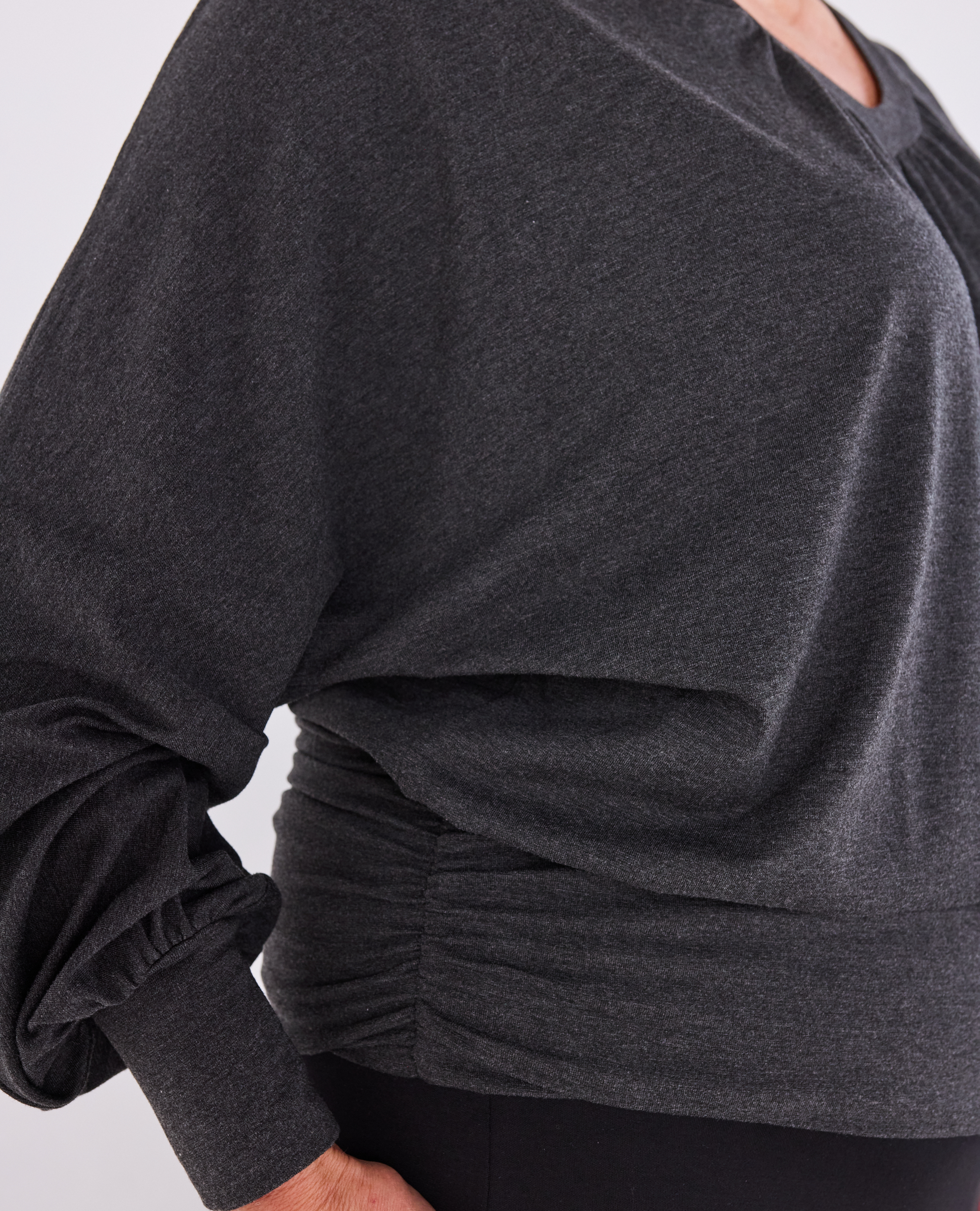 Close-up of a dark charcoal grey heathered long-sleeve Melyr Vivienne top with a gathered ruched waist and elbow-length sleeves, worn by a model.