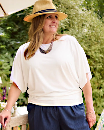 Woman wearing a Melyr  Nico white top and navy shorts with a straw hat outdoors.
